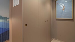 Un couloir avec une porte beige, une œuvre d’art encadrée au mur et une zone carrelée sur la gauche.