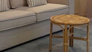 Un salon avec un canapé, des coussins à rayures, une petite table d’appoint en osier, une lampe bleue et blanche, et un mur recouvert de carreaux.