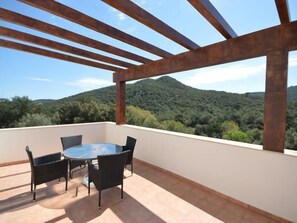 A balcony with a round table and chairs, a view of a forested mountain range, and a clear sky. - Spectacular Luxury Villa with Private Garden Near the Sea (Calonge i Sant Antoni)