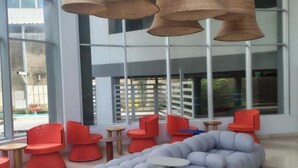 A modern interior with large windows, wicker pendant lights, and a mix of red and grey seating. - Oceani Cartagena (La Boquilla)