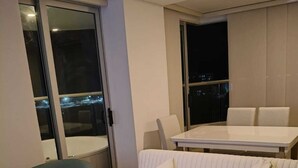 A modern living room with a sofa, a dining table, and a chair. There is a sliding glass door leading to a balcony with a city view. - Oceani Cartagena (La Boquilla)