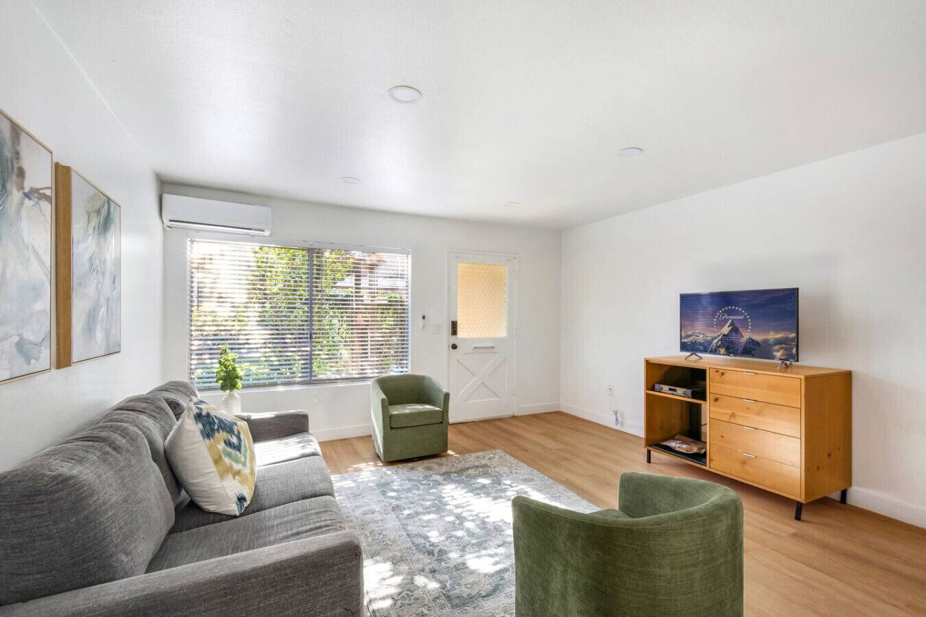 A spacious living room with a grey sofa, a green armchair, a wooden cabinet, and a television on a stand.