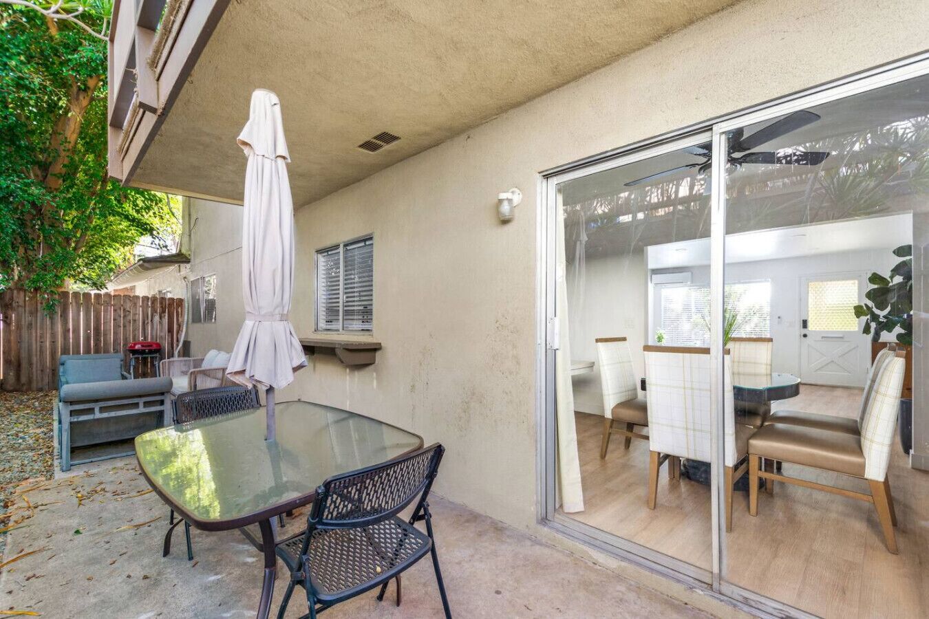 A patio area with a glass door leading to an indoor dining space, a table with chairs, and a covered seating area.