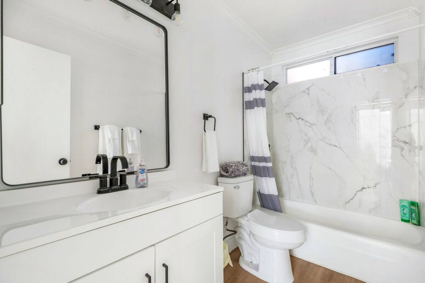 A modern bathroom with a white vanity, a large mirror, a toilet, and a shower with a marble wall.