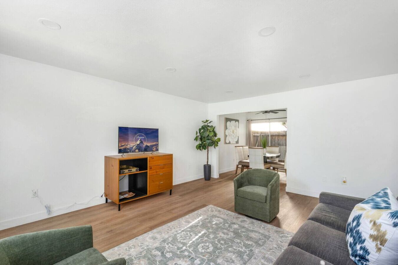 A modern living room with a wooden cabinet, a green armchair, a grey sofa, and a patterned rug.