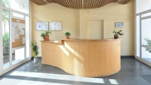 A reception desk with a wooden slatted ceiling, potted plants, and framed informational posters on the wall. - Ground Floor Apt with Terrace & Pool Near Beach (ROSES)