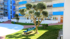 A courtyard with a tree, a bench, and a building with balconies. - Ground Floor Apt with Terrace & Pool Near Beach (ROSES)