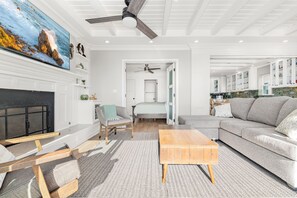 A spacious living room with a fireplace, a sofa, a coffee table, and a painting of a coastal scene. - 3BR Beachfront Home, Patio on the Sand w/ Gorgeous Ocean Views! (Newport Beach)