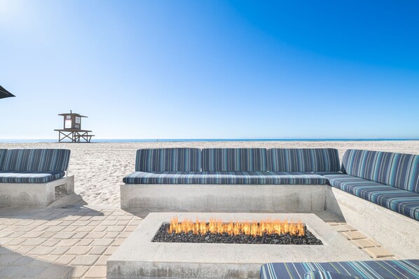 A beachside seating area with a fire pit, a lifeguard tower, and a clear view of the ocean. - 3BR Beachfront Home, Patio on the Sand w/ Gorgeous Ocean Views! (Newport Beach)