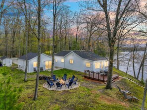 A lakeside cabin with a deck, outdoor seating, and a fire pit. - Lakefront Cottage, Dock, EV Charger, Firepit, Bunkhouse, Family & Pet Friendly (Carp Lake)