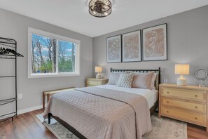 A bedroom with a bed, bedside tables, a lamp, a bench, a coat rack, and framed artwork on the wall. - Lakefront Cottage, Dock, EV Charger, Firepit, Bunkhouse, Family & Pet Friendly (Carp Lake)