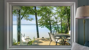 Une pièce dotée d’une grande fenêtre donnant sur un lac, d’une terrasse en bois et de mobilier d’extérieur.