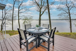 A round table with chairs on a wooden deck, overlooking a calm lake with trees in the background. - Lakefront Cottage, Dock, EV Charger, Firepit, Bunkhouse, Family & Pet Friendly (Carp Lake)