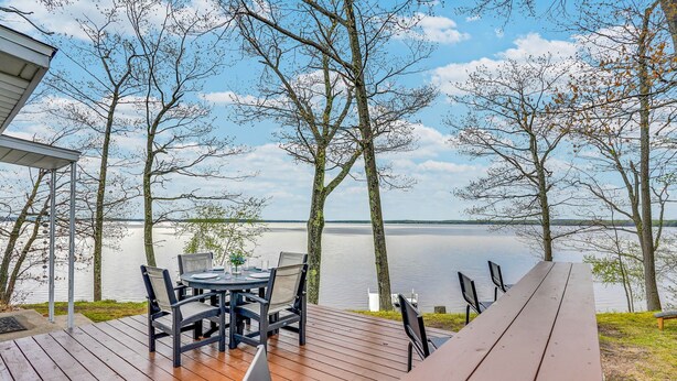 Une terrasse en bois avec une table et des chaises donnant sur un lac paisible.