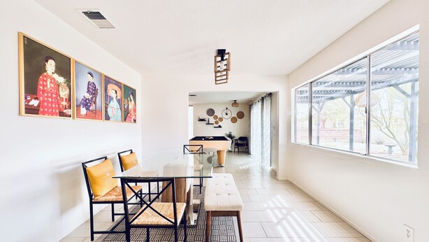 A modern dining area with a glass table, black chairs, and a patterned rug. There are framed artworks on the wall and a view of the outdoors through large windows. - 5 mins to STRIP & LAS Airport, 3 King Bed 2.5 Bath, Peaceful & Clean (Las Vegas)