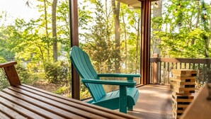 Ett trädäck med en grön Adirondack-stol och ett bord, omgivet av en utsikt över en skog.
