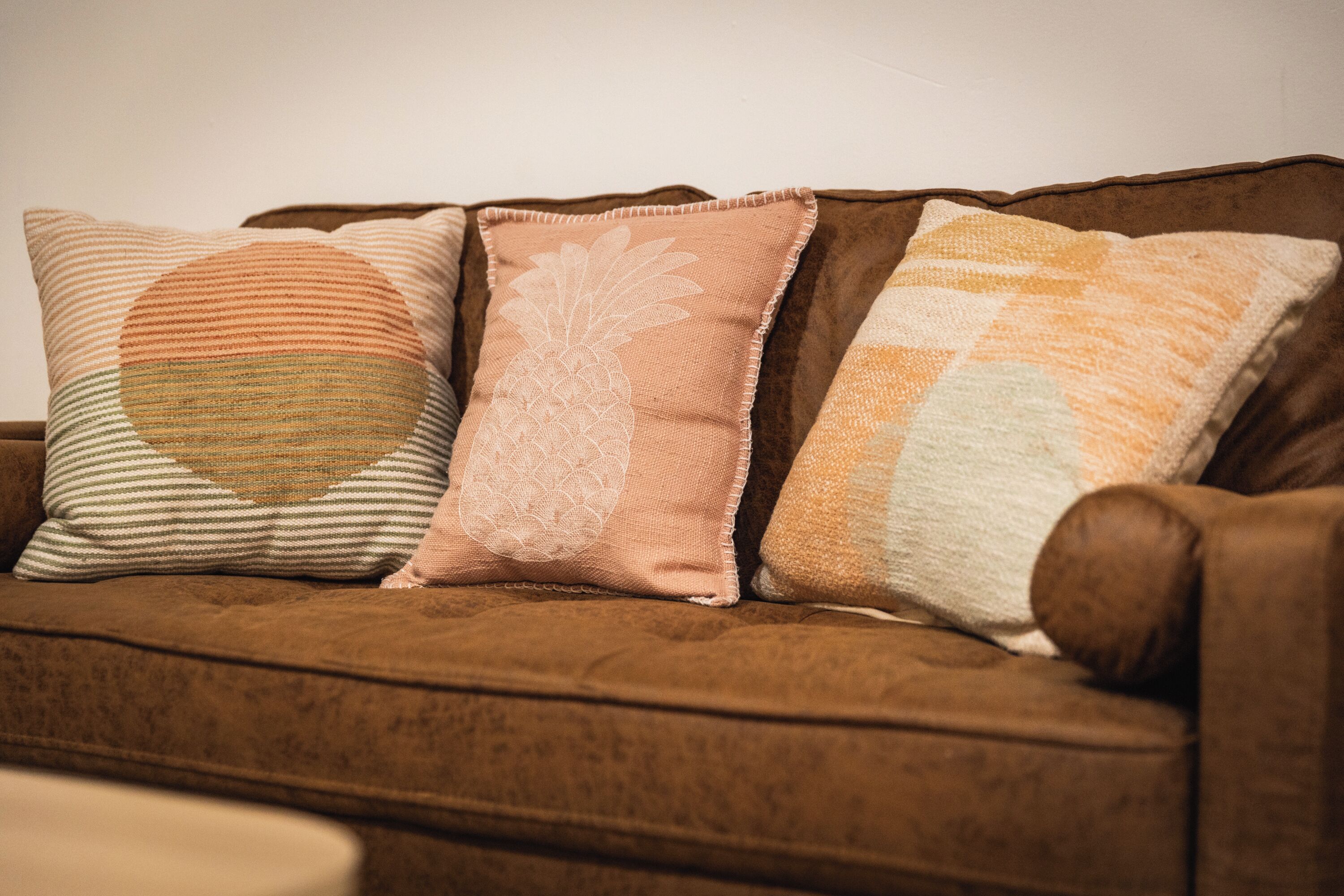 Een bruine bank met drie decoratieve kussens.