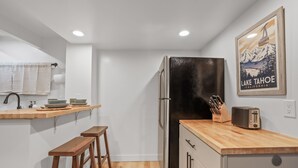 A compact kitchen with a black refrigerator, wooden countertop, and bar stools.