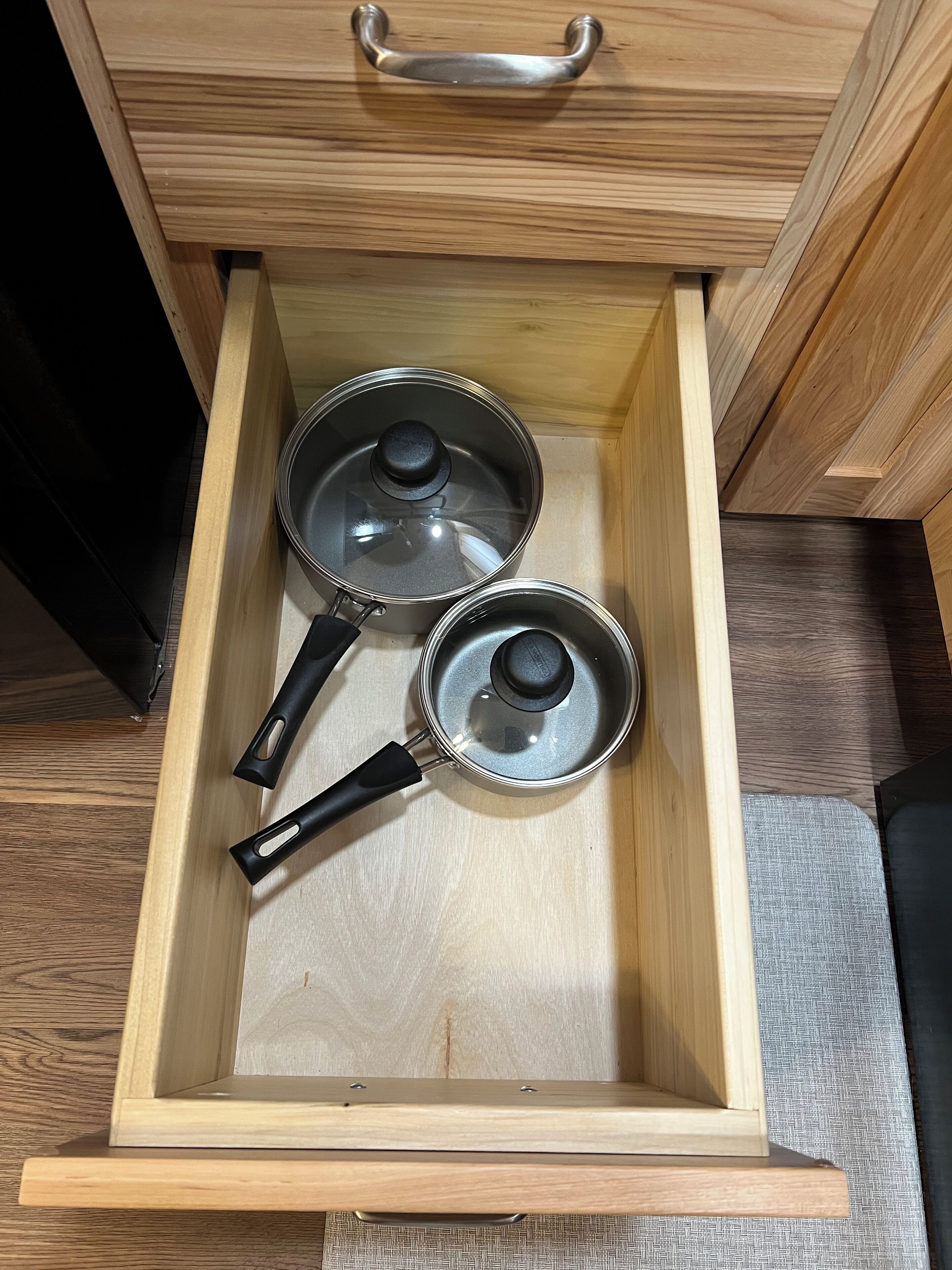 A wooden drawer with two metal pots and a black handle.