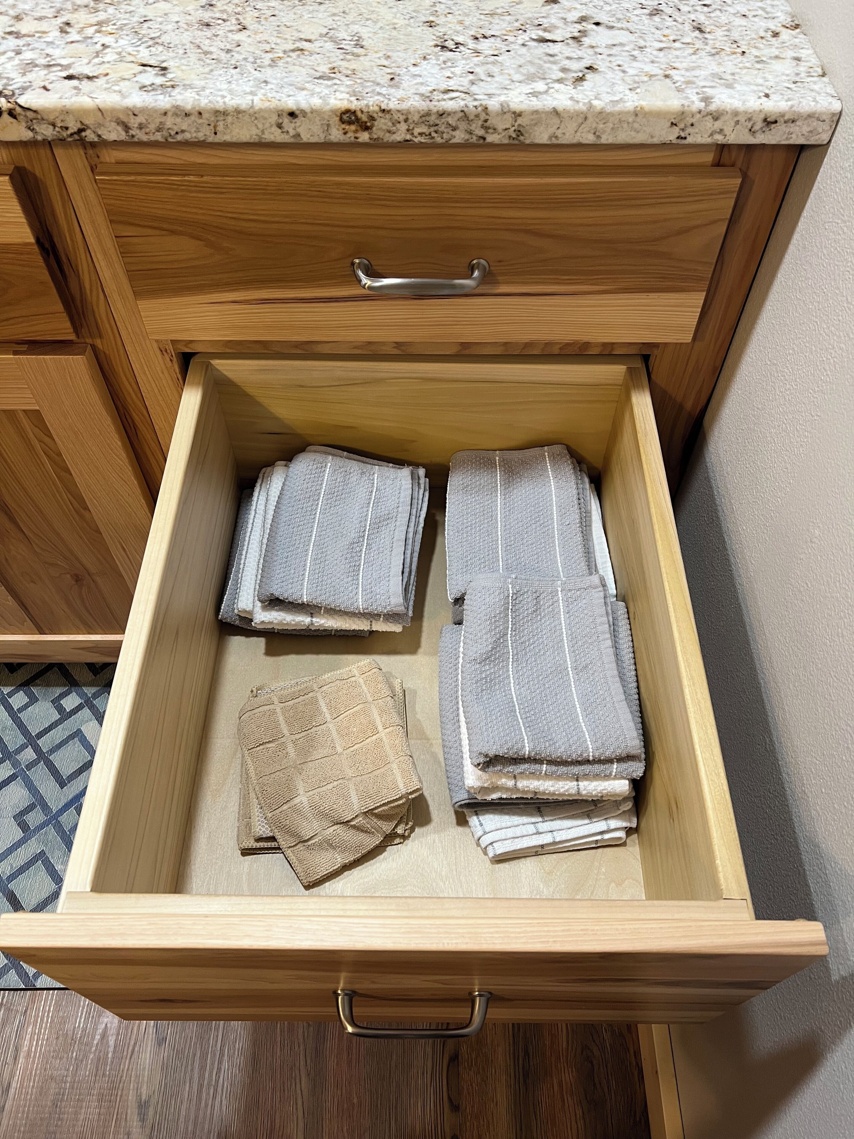 A wooden drawer with a handle, containing folded towels and a woven cloth.