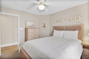 A bedroom with a bed, a nightstand, a dresser, a ceiling fan, and a wall sign that reads 'ABSOLUTE BEACH'. - 5BR North End Beach Retreat w/ Porch, Garage & Outdoor Shower (Ocean City)