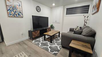 A modern living room with a flat-screen TV, a grey sofa, wooden coffee tables, and patterned rugs.