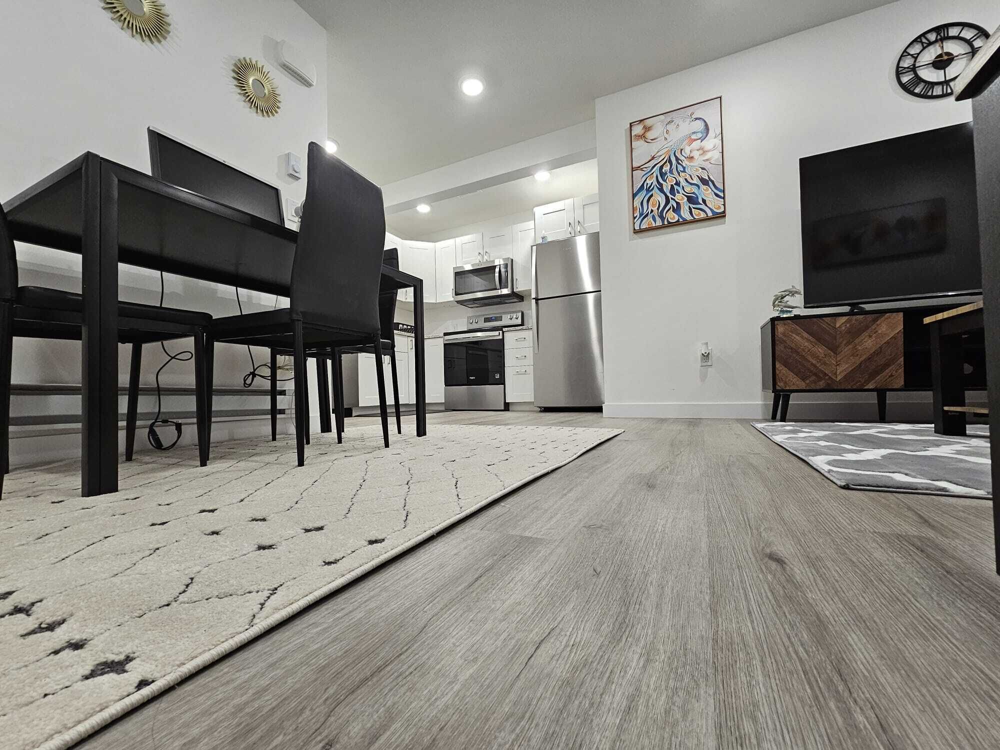 A modern kitchen with a dining area, featuring a black dining table and chairs, a stainless steel refrigerator, and a microwave.