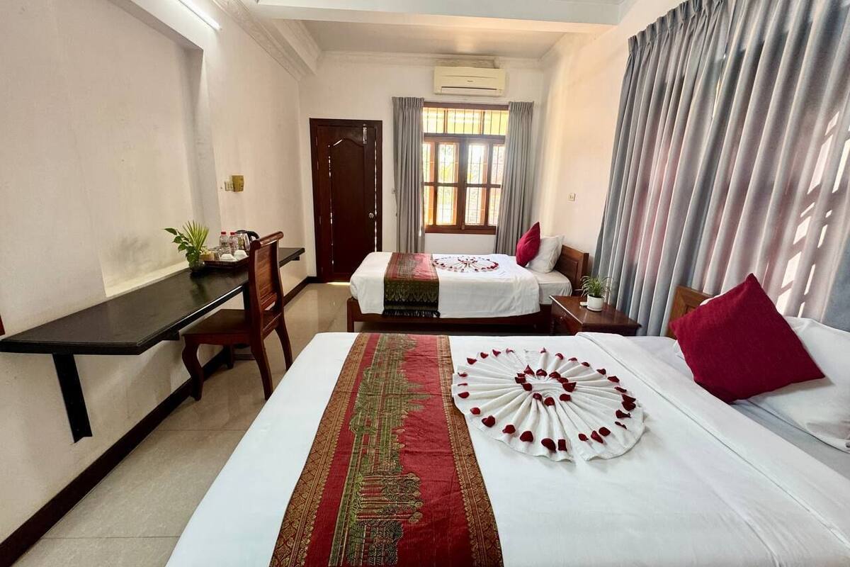 Ein Hotelzimmer mit einem großen Bett, einem Schreibtisch und einem Stuhl. Es gibt ein Fenster mit Vorhängen und eine Klimaanlage an der Wand.