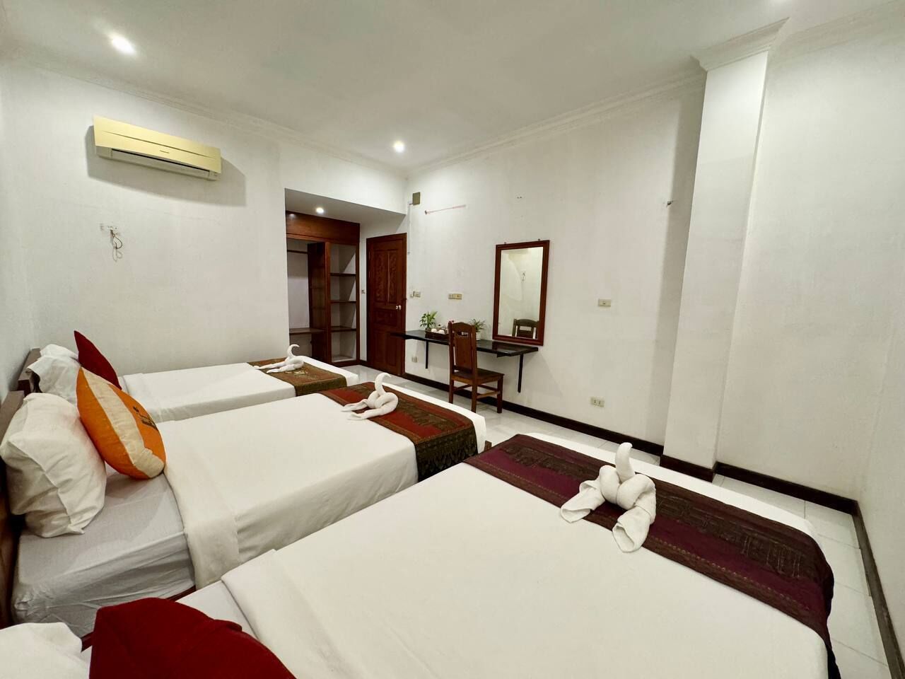 A hotel room with four single beds, a desk, a chair, a mirror, and an air conditioning unit.