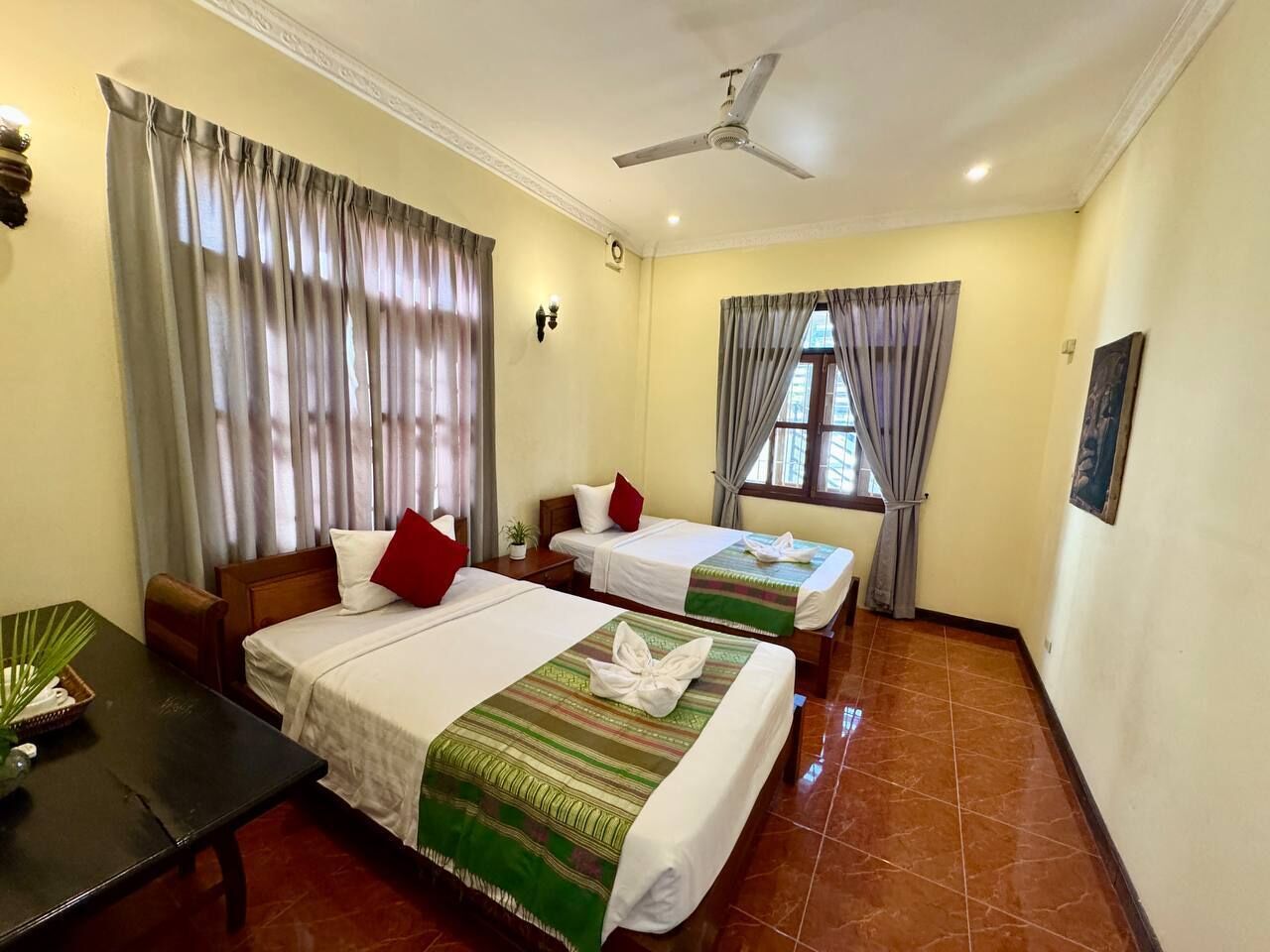 A hotel room with two beds, a desk, a chair, a ceiling fan, and a window with curtains.