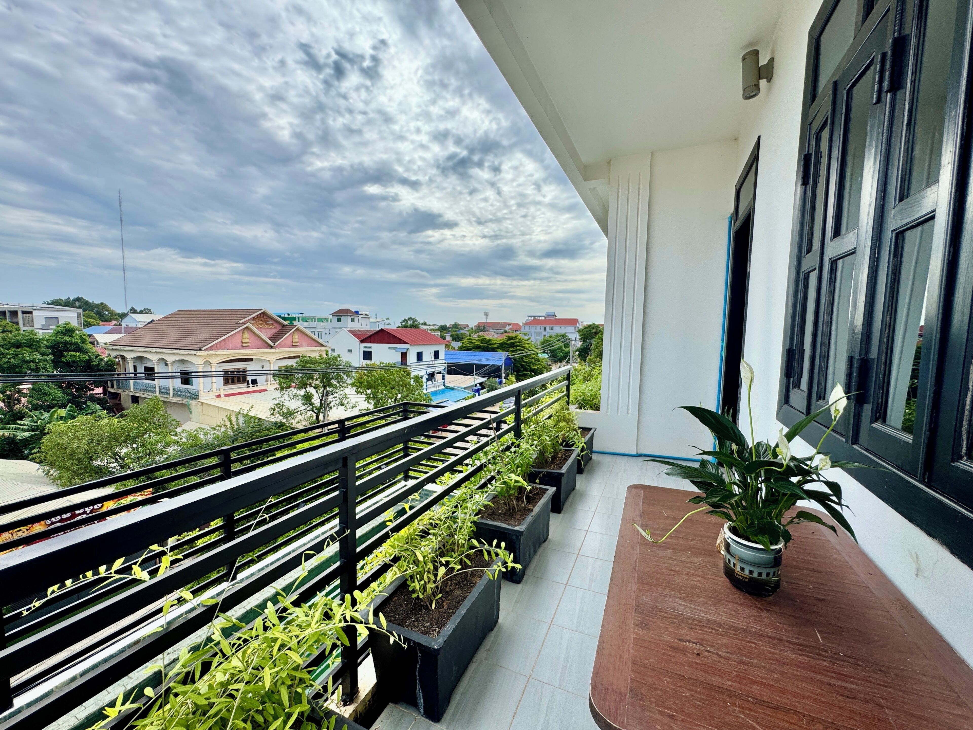 A balcony with a railing, potted plants, and a view of the neighborhood.