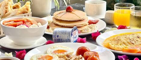 A breakfast table with pancakes, eggs, bacon, sausages, and a variety of fruits and beverages.
