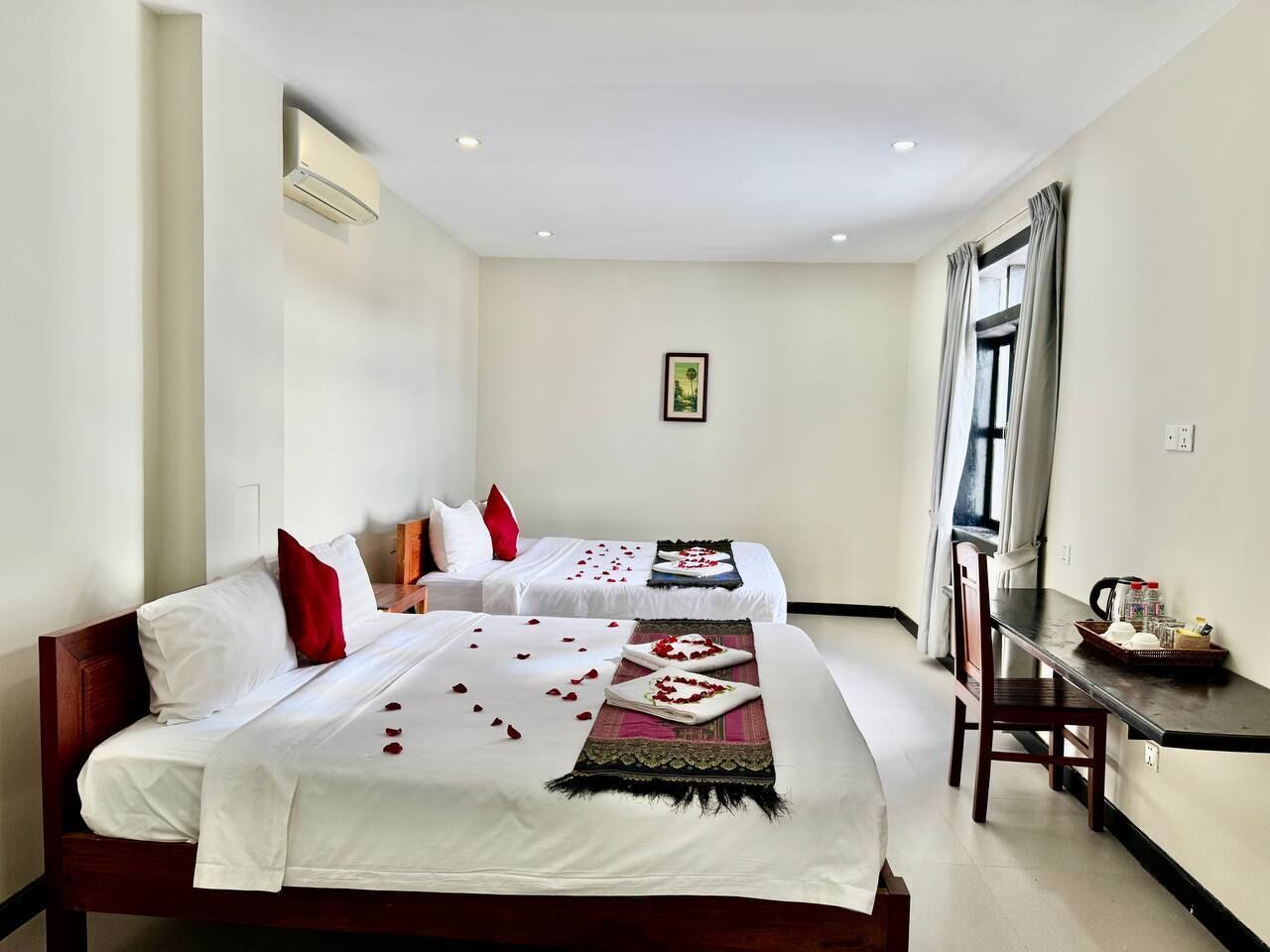 A hotel room with two beds, a dining table, and a window with curtains.