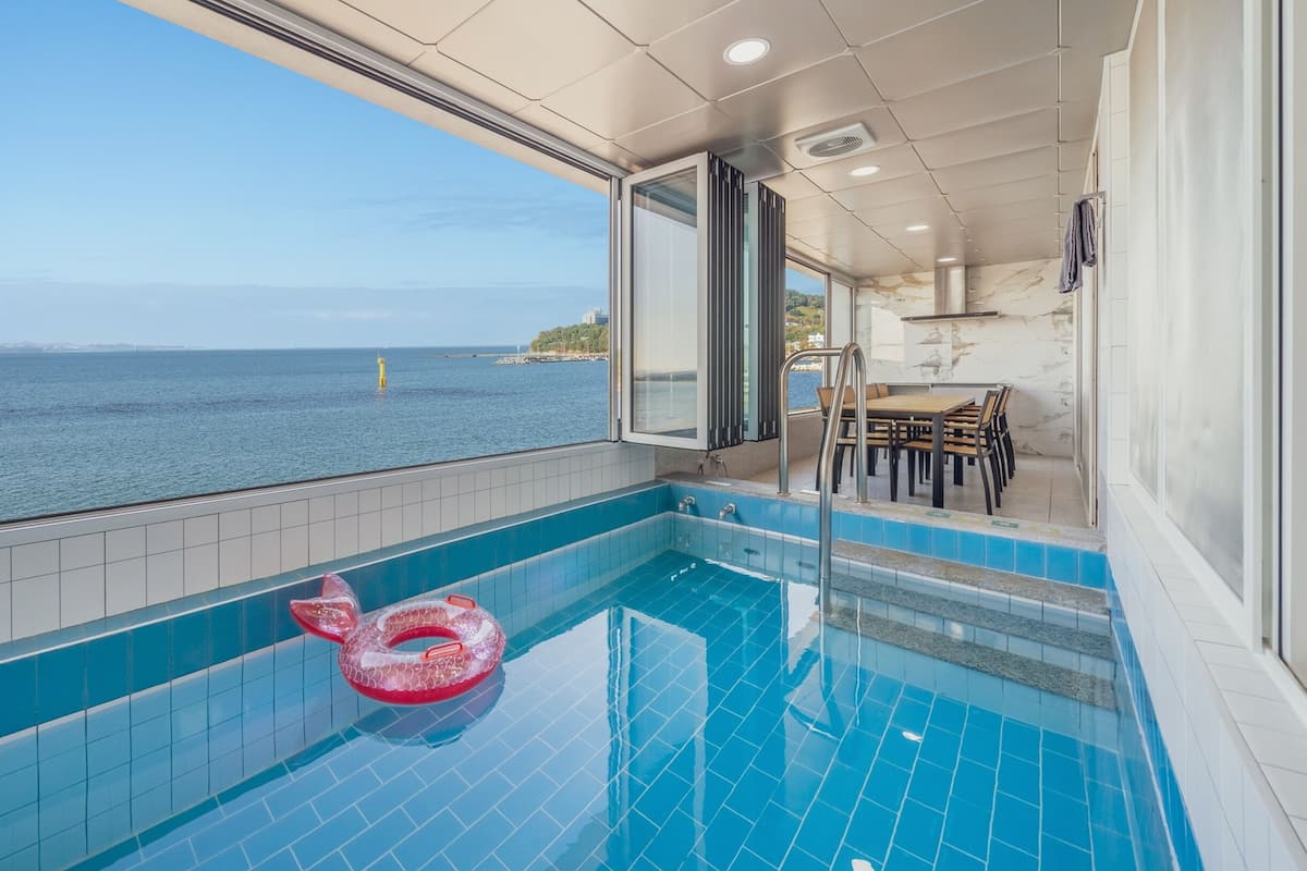 A pool with a view of the sea, a dining area, and a staircase leading to an upper deck.