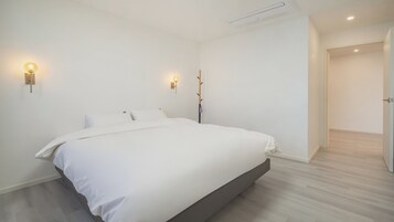 Un dormitorio minimalista con una cama grande, dos lámparas fijadas a la pared y suelo de madera.