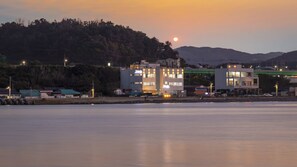 A waterfront property with modern buildings, a visible road, and a hill in the background. - Pohang Luna Ocean View Pool Villa (Pohang)