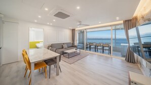 A modern living room with a dining area, a sofa, a coffee table, and a view of the sea through large windows. - Pohang Luna Ocean View Pool Villa (Pohang)
