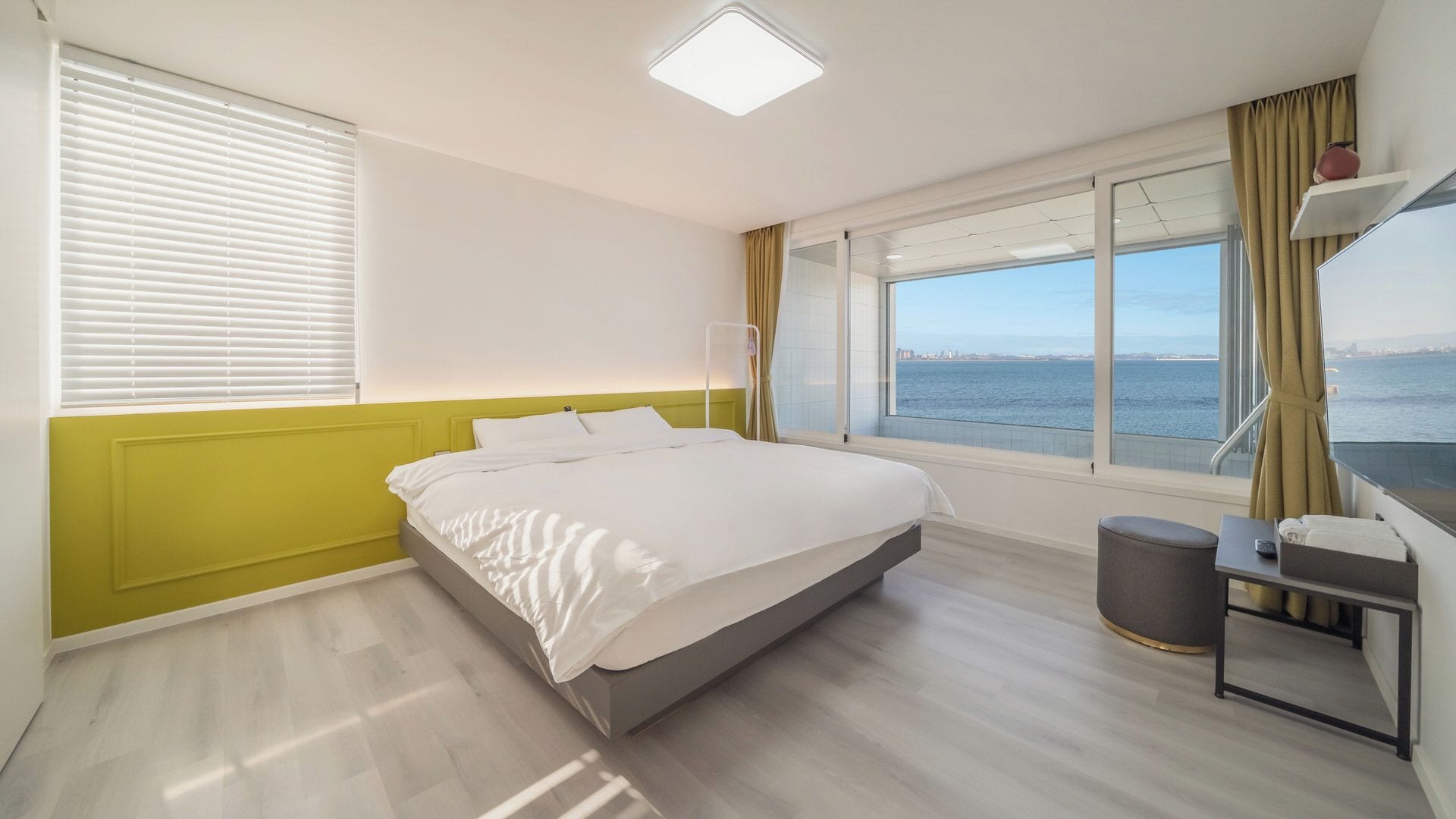 Una habitación de hotel con una cama, un ventanal con vista al mar, una mesita de noche y una silla.