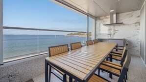 A dining area with a long wooden table and chairs, large windows with a view of the sea and a distant shoreline. - Pohang Luna Ocean View Pool Villa (Pohang)