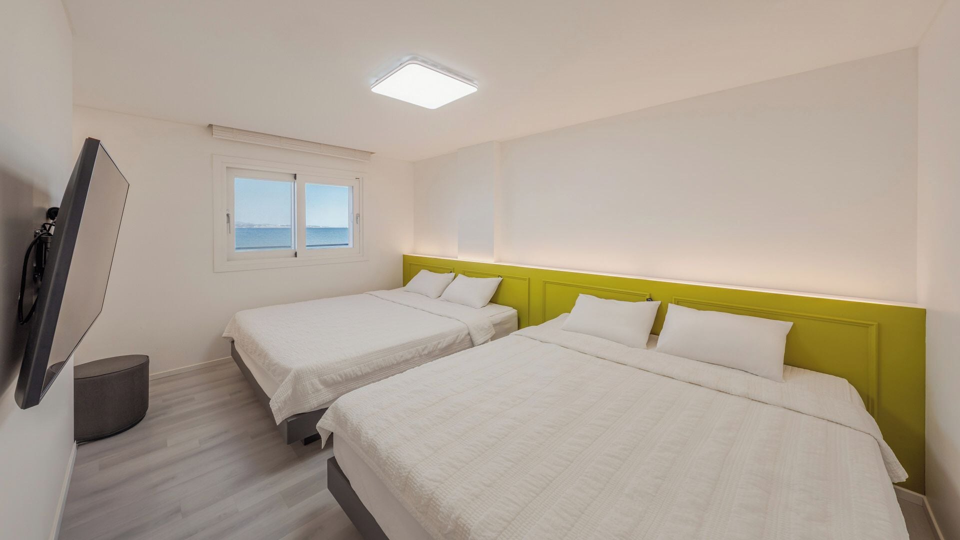 A hotel room with two beds, a window with a view, and a flat-screen TV mounted on the wall.