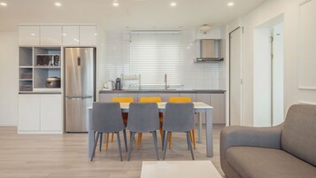 Una cocina moderna con refrigerador empotrado, una mesa de comedor con sillas y un sofá en la sala.