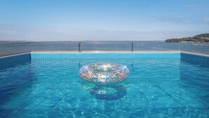 A clear blue pool with a decorative inflatable ring in the center, surrounded by a tiled deck and a view of the sea. - Pohang Luna Ocean View Pool Villa (Pohang)