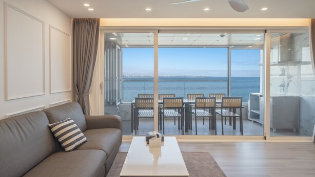 A modern living room with a sofa, a coffee table, and a view of the sea through large glass doors. - Pohang Luna Ocean View Pool Villa (Pohang)