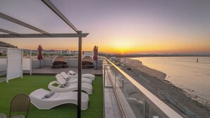 A rooftop terrace with lounge chairs, a small seating area, and a view of the sunset over the sea. - Pohang Luna Ocean View Pool Villa (Pohang)