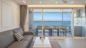 Een moderne woonkamer met een bank, een bijzettafeltje en uitzicht op zee door grote glazen deuren.