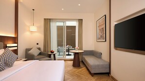 Une chambre d’hôtel avec un lit, deux canapés, une petite table avec un vase et un téléviseur fixé au mur.