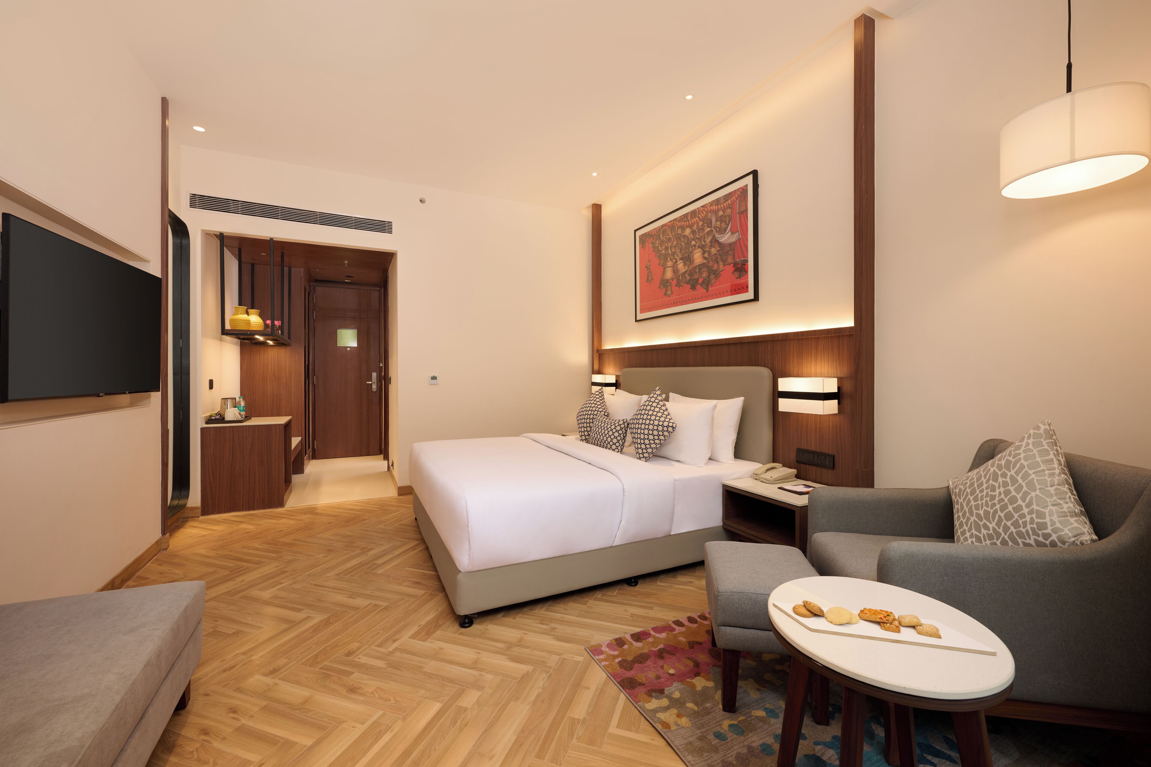 Une chambre d’hôtel avec un lit, un canapé, une petite table avec des collations, une télévision et un tableau au mur.