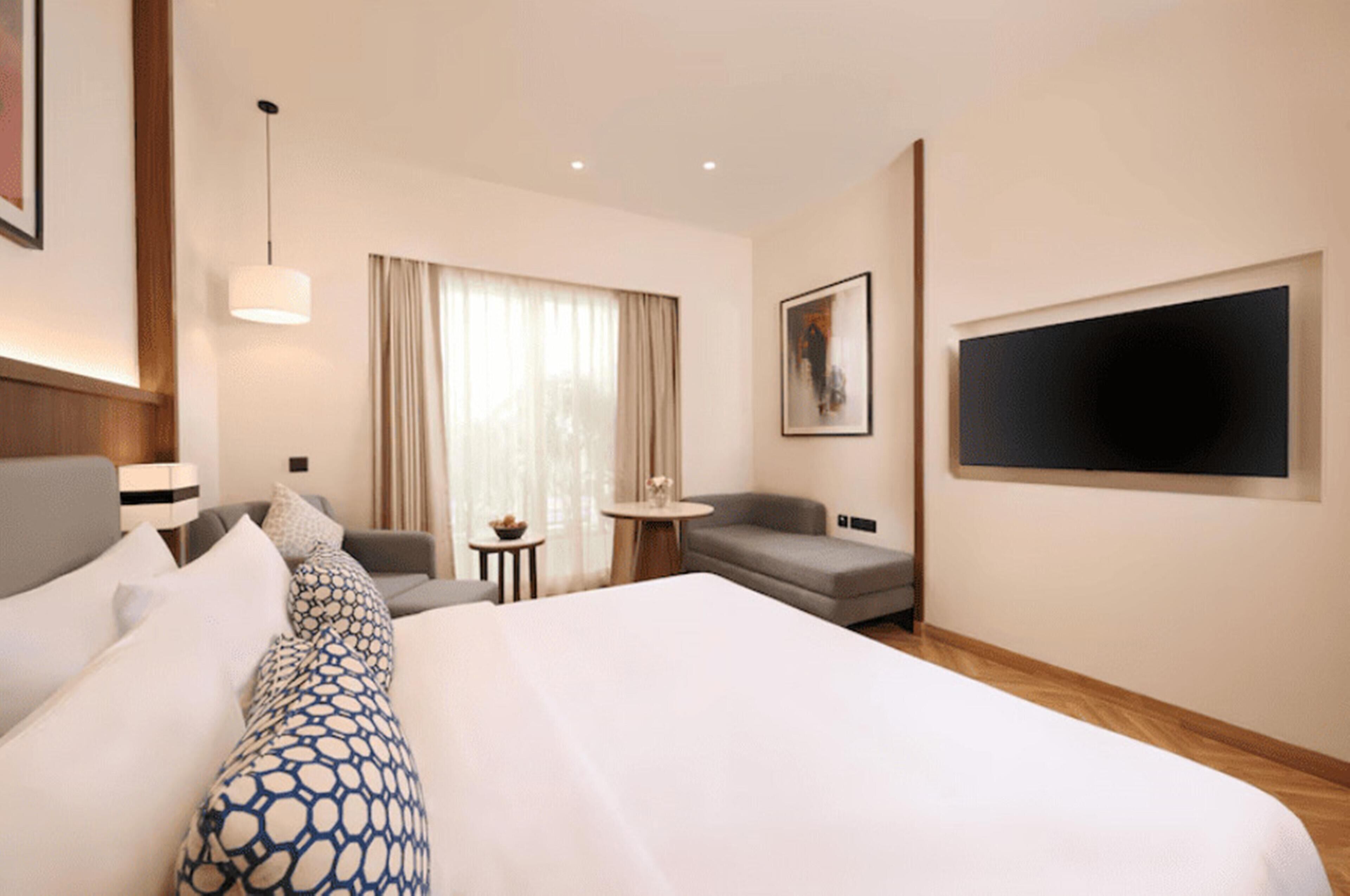 Habitación de hotel con una cama grande, un sofá, una mesita, un televisor y una ventana con cortinas.