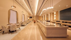 Un hall d’hôtel moderne avec un long comptoir d’accueil, plusieurs espaces de détente et un grand tableau noir sur le mur de droite.