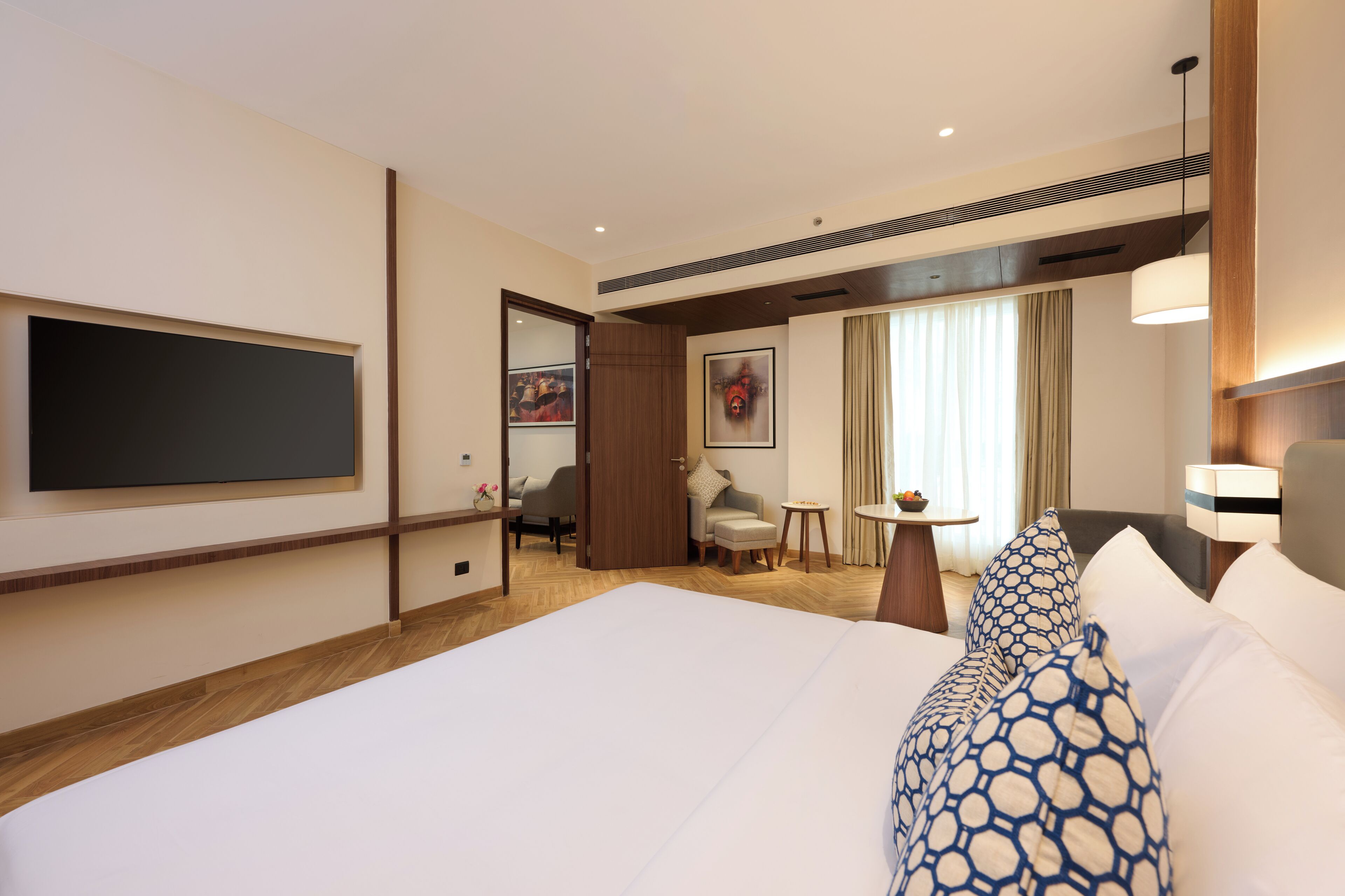 Une chambre d’hôtel avec un grand lit, un téléviseur fixé au mur, un bureau avec une chaise et une petite table avec une lampe.